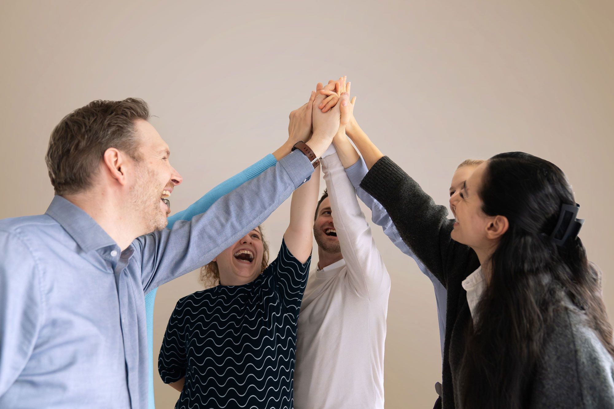 Team gibt sich lachend High-Five im Büro – Symbol für Zusammenarbeit und Erfolg im Unternehmen