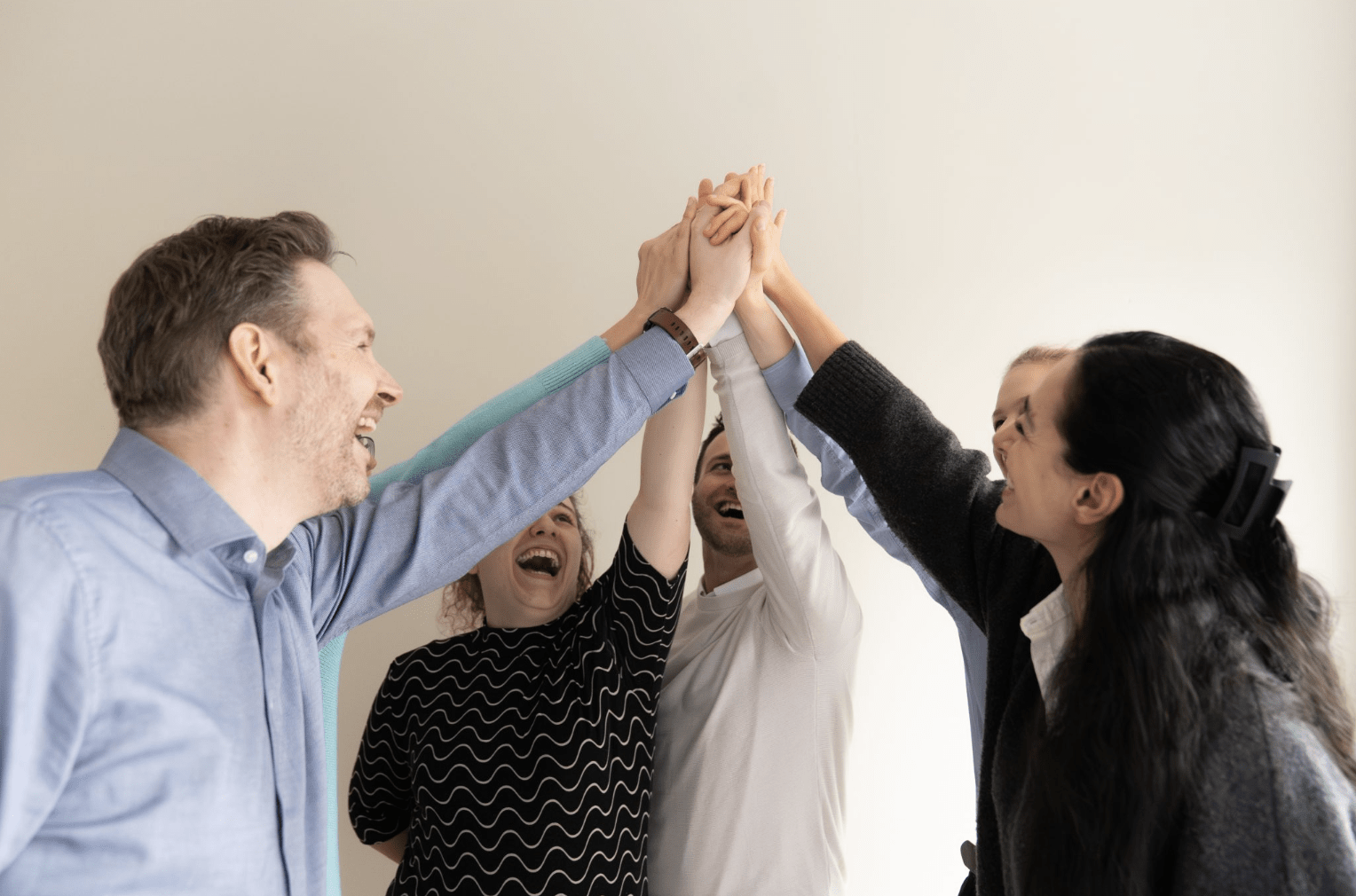 Team gibt sich lachend High-Five im Büro – Symbol für Zusammenarbeit und Erfolg im Unternehmen