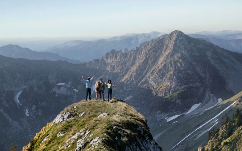 Bergsteigergruppe auf Gipfelgrat blickt jubelnd über Alpenpanorama – Symbolbild für Veränderung und Erfolg