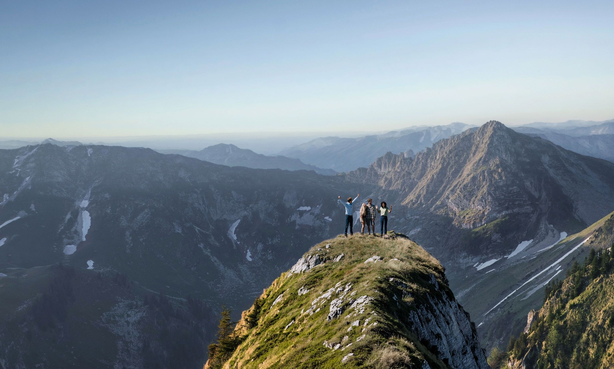 Bergsteigergruppe auf Gipfelgrat blickt jubelnd über Alpenpanorama – Symbolbild für Veränderung und Erfolg